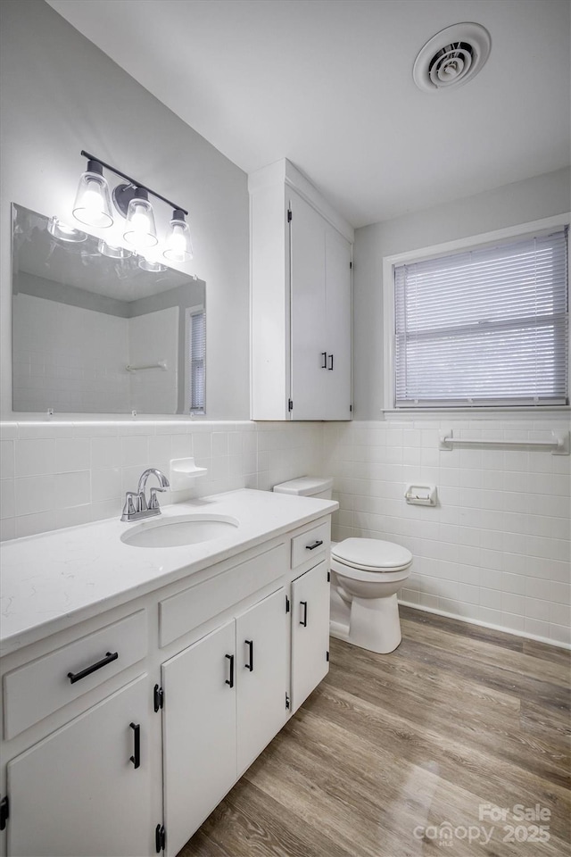 bathroom featuring toilet, wood finished floors, vanity, visible vents, and tile walls