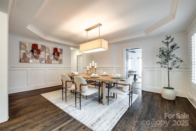 dining space featuring crown molding, a decorative wall, and dark wood finished floors