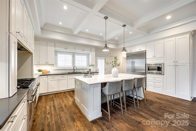 kitchen with a center island, a breakfast bar area, hanging light fixtures, a sink, and built in appliances