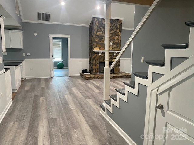 interior space with a fireplace, wood finished floors, visible vents, stairs, and ornamental molding