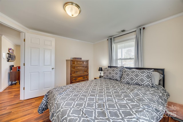 bedroom with ornamental molding, visible vents, and wood finished floors