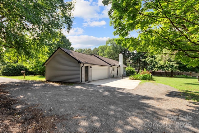 view of side of property with a garage, fence, a yard, driveway, and a chimney