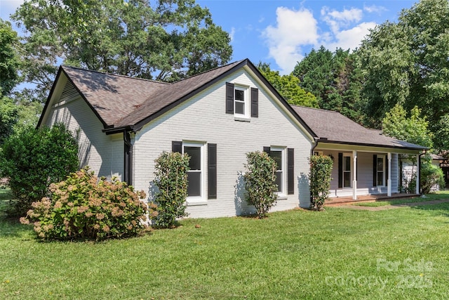 view of front of property featuring covered porch, roof with shingles, brick siding, and a front lawn