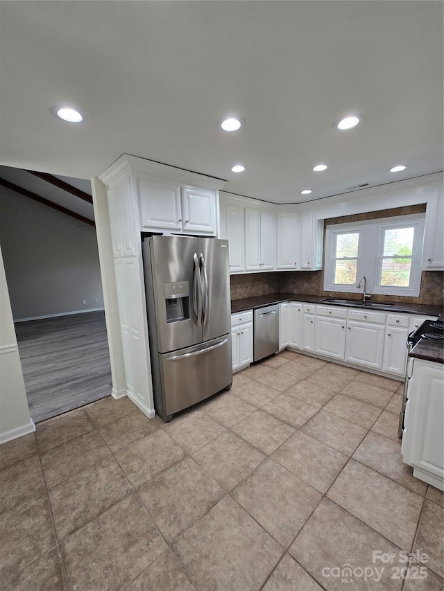 kitchen featuring tasteful backsplash, dark countertops, appliances with stainless steel finishes, white cabinets, and a sink