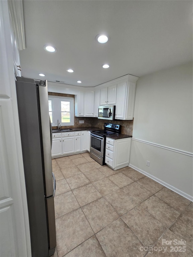 kitchen with decorative backsplash, dark countertops, appliances with stainless steel finishes, white cabinetry, and a sink