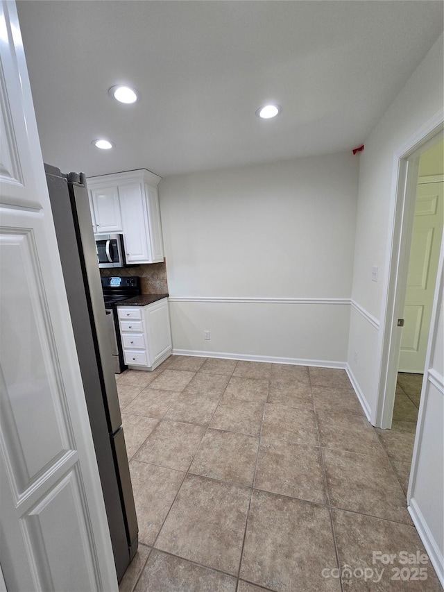 kitchen featuring stainless steel microwave, electric range, backsplash, white cabinets, and baseboards