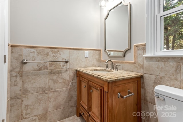 bathroom with tile walls, wainscoting, vanity, and toilet