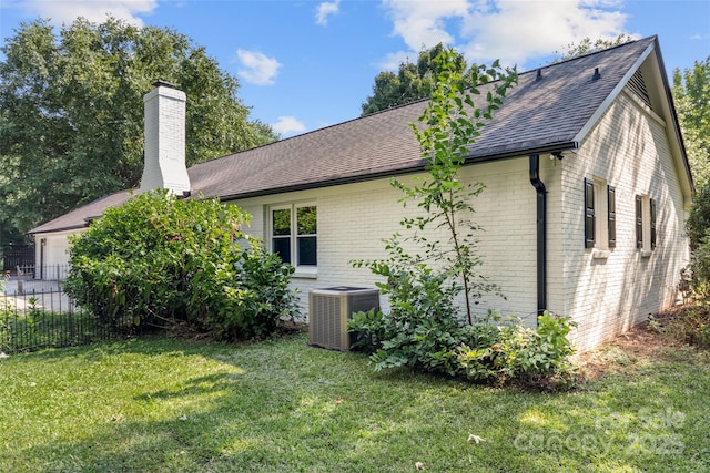 view of side of home with a chimney, roof with shingles, cooling unit, a yard, and brick siding