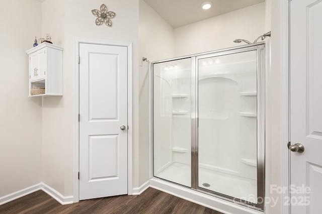 bathroom featuring wood finished floors, a shower stall, and baseboards