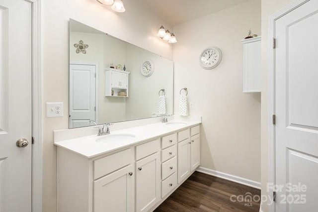 bathroom with double vanity, wood finished floors, a sink, and baseboards