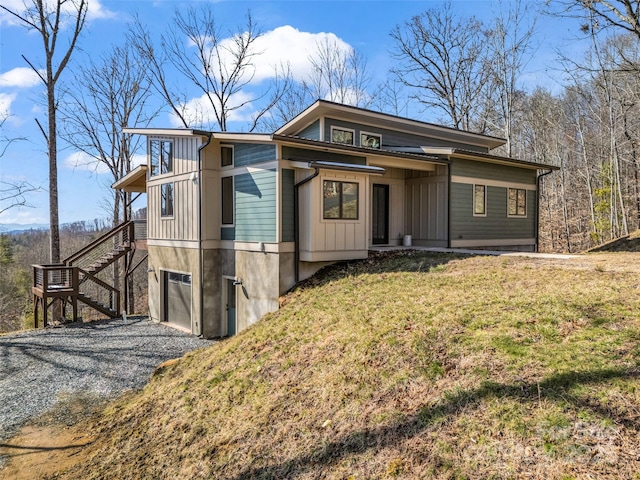 view of front facade featuring driveway, stairway, an attached garage, a front lawn, and board and batten siding