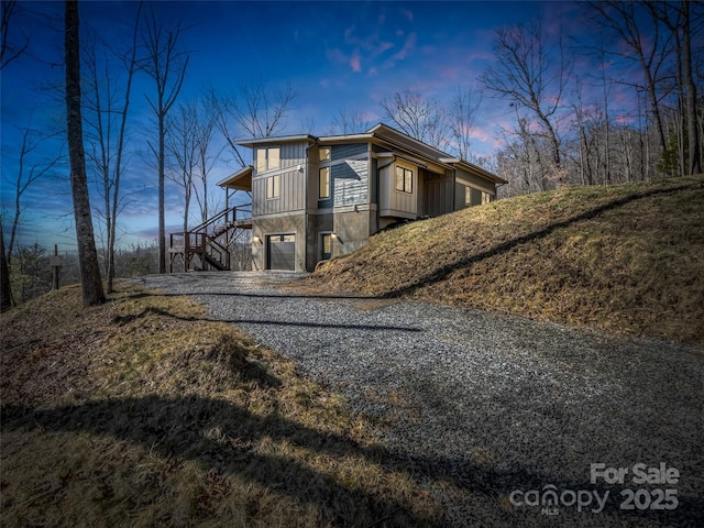 property exterior at dusk with gravel driveway, a garage, stairs, and board and batten siding