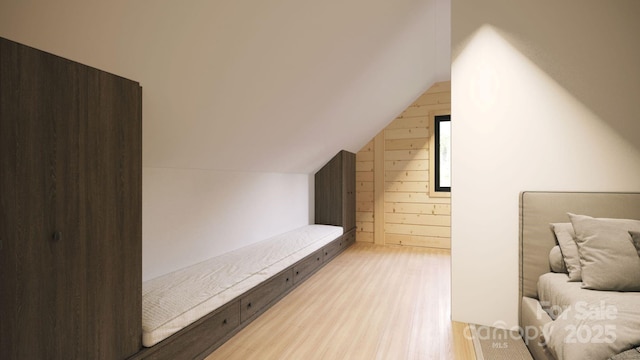 bedroom with light hardwood / wood-style flooring, wood walls, and lofted ceiling