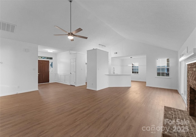 unfurnished living room featuring a ceiling fan, visible vents, a fireplace, and wood finished floors