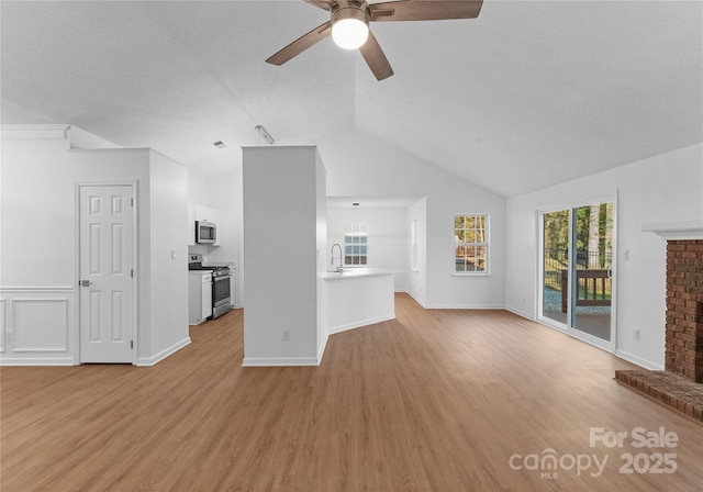 unfurnished living room with lofted ceiling, a sink, a ceiling fan, a brick fireplace, and light wood finished floors