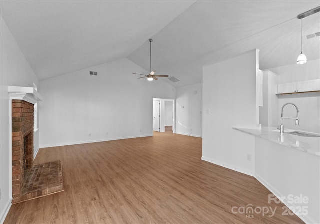 unfurnished living room with visible vents, a ceiling fan, light wood-style floors, a brick fireplace, and a sink