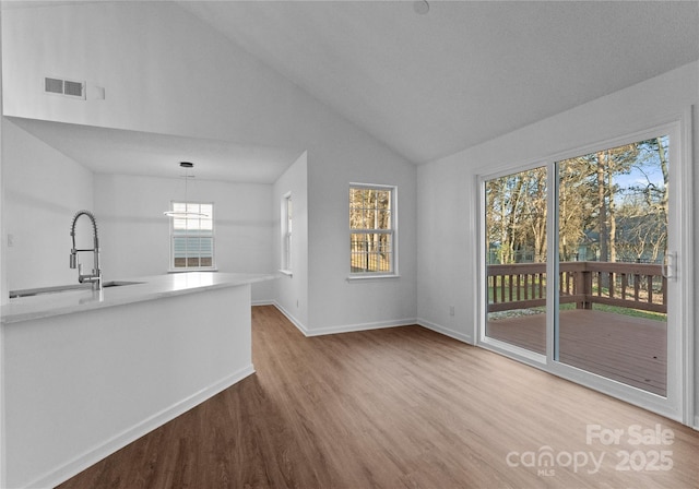 unfurnished living room with visible vents, vaulted ceiling, a sink, wood finished floors, and baseboards