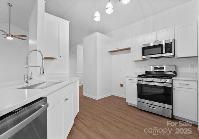 kitchen with stainless steel appliances, wood finished floors, a sink, white cabinetry, and light countertops