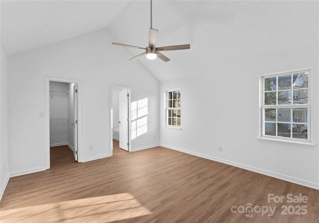 unfurnished bedroom with a walk in closet, a closet, a ceiling fan, wood finished floors, and baseboards