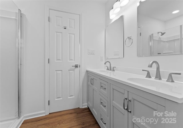 full bath with a shower, double vanity, a sink, and wood finished floors