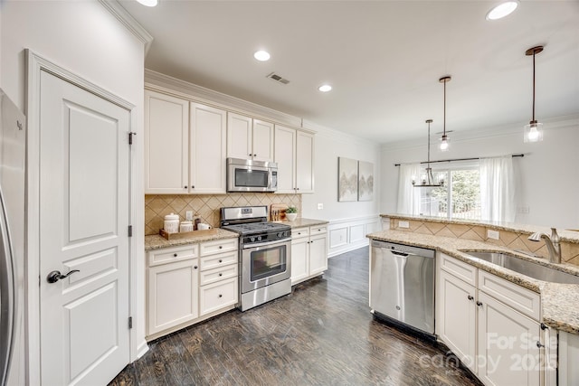 kitchen featuring pendant lighting, visible vents, appliances with stainless steel finishes, ornamental molding, and a sink