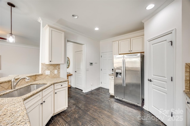 kitchen with a sink, ornamental molding, stainless steel refrigerator with ice dispenser, light stone countertops, and decorative light fixtures