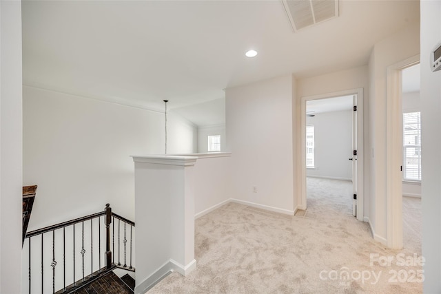 hallway featuring baseboards, visible vents, light carpet, and an upstairs landing