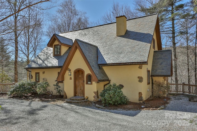 tudor home with a high end roof, a chimney, and stucco siding