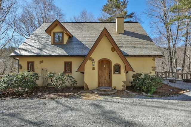 tudor-style house with a chimney, a high end roof, and stucco siding