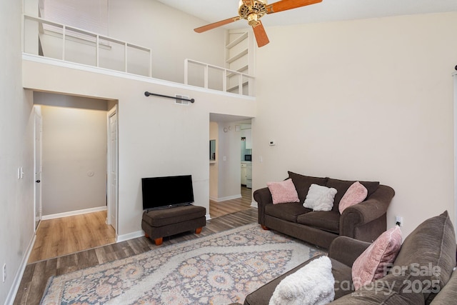 living room featuring a ceiling fan, a high ceiling, baseboards, and wood finished floors