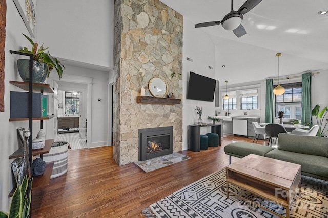 living room featuring a stone fireplace, wood finished floors, a wealth of natural light, and a ceiling fan