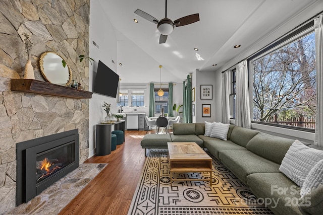 living area featuring visible vents, ceiling fan, wood finished floors, a stone fireplace, and high vaulted ceiling