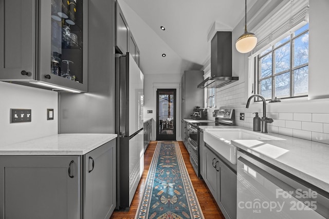 kitchen featuring gray cabinetry, appliances with stainless steel finishes, wall chimney range hood, dark wood-style floors, and glass insert cabinets