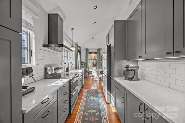 kitchen with range with two ovens, gray cabinets, a sink, wood finished floors, and wall chimney exhaust hood