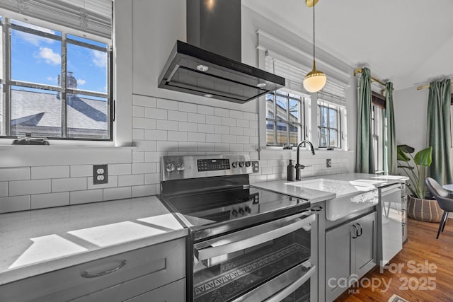 kitchen with stainless steel appliances, gray cabinets, wall chimney exhaust hood, and wood finished floors