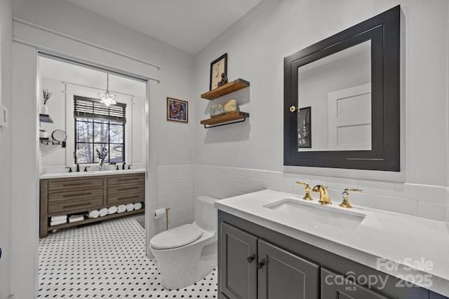 bathroom with toilet, wainscoting, vanity, and tile walls