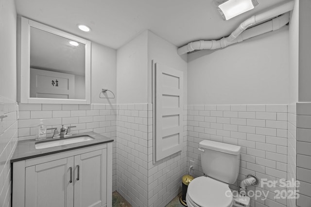 bathroom with visible vents, toilet, vanity, tile walls, and recessed lighting