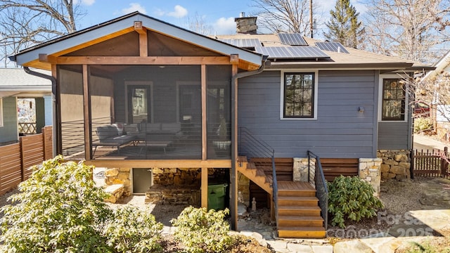 back of house with a chimney, solar panels, stairway, a sunroom, and fence