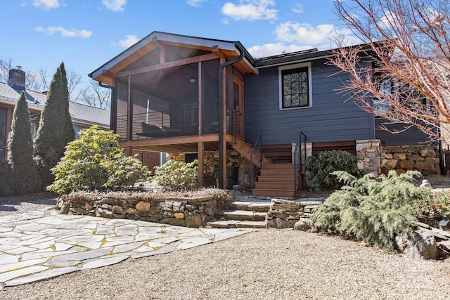 rear view of property featuring a sunroom, stone siding, stairway, and a patio