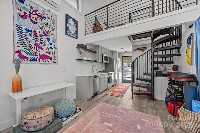 bar featuring light wood finished floors, stainless steel appliances, a towering ceiling, baseboards, and stairs