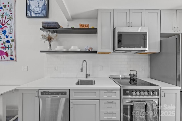 kitchen with open shelves, tasteful backsplash, light countertops, appliances with stainless steel finishes, and a sink