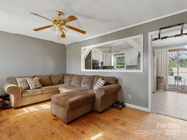 living area featuring a textured ceiling, ceiling fan, wood finished floors, baseboards, and ornamental molding