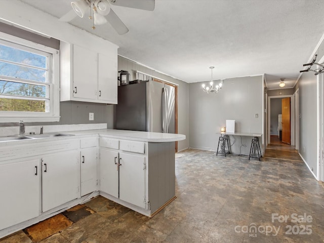 kitchen with white cabinets, freestanding refrigerator, a peninsula, light countertops, and a sink