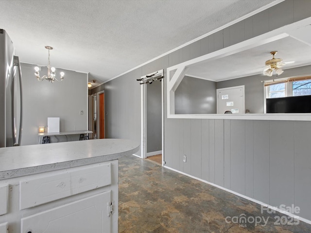 kitchen with a textured ceiling, ceiling fan with notable chandelier, wood walls, white cabinetry, and light countertops