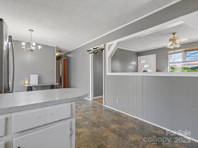 kitchen featuring light countertops, white cabinetry, wood walls, a textured ceiling, and ceiling fan with notable chandelier