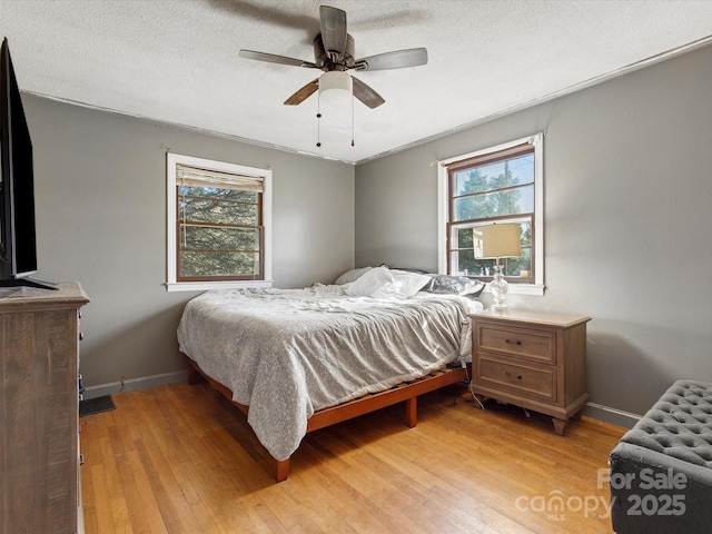 bedroom featuring light wood-style flooring, baseboards, ceiling fan, and a textured ceiling