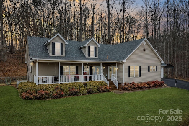 cape cod home with covered porch, roof with shingles, aphalt driveway, and a lawn