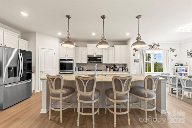 kitchen featuring appliances with stainless steel finishes, white cabinetry, hanging light fixtures, and an island with sink