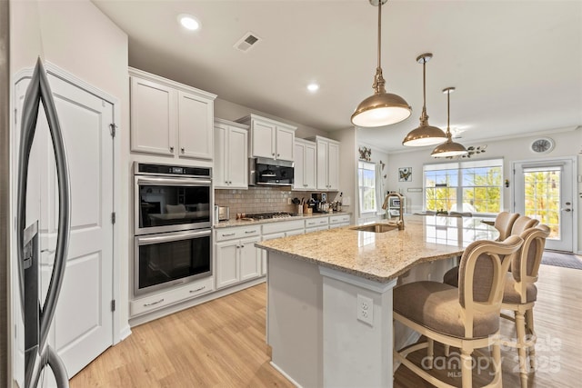 kitchen with appliances with stainless steel finishes, a sink, decorative light fixtures, and white cabinets