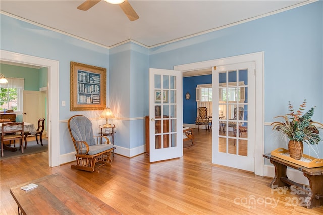 living area featuring a ceiling fan, baseboards, ornamental molding, french doors, and light wood-type flooring